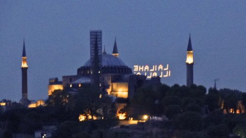 Back view of Hagia Sophia church exterior at night with light decorations between its minarets titles in Turkish "There's no God but Allah"